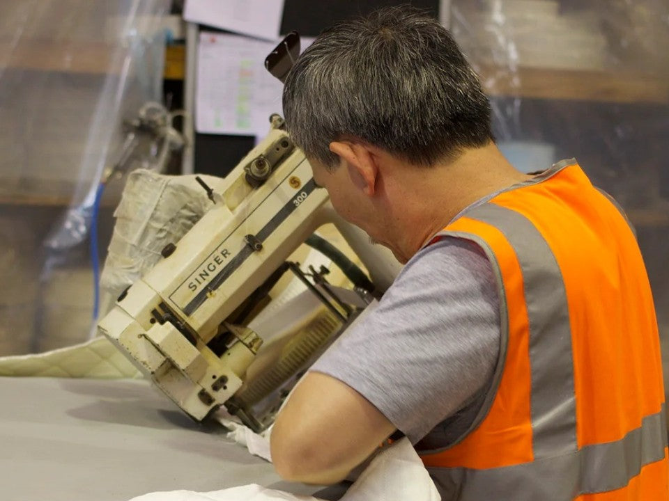 A machinist closing the tape edge of a mattress on a Singer closer in the Sleep Collective factory