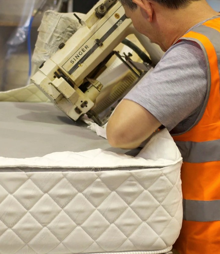 A worker guiding a quilted mattress panel through a machine in an Australian factory